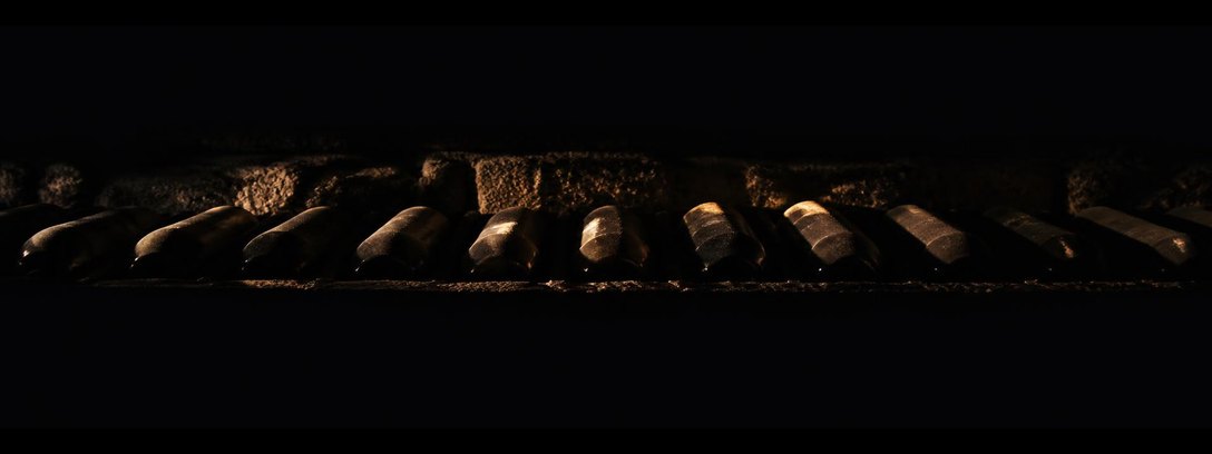 Bottles lying in a stone cellar niche, a single grazing light across their shoulders.