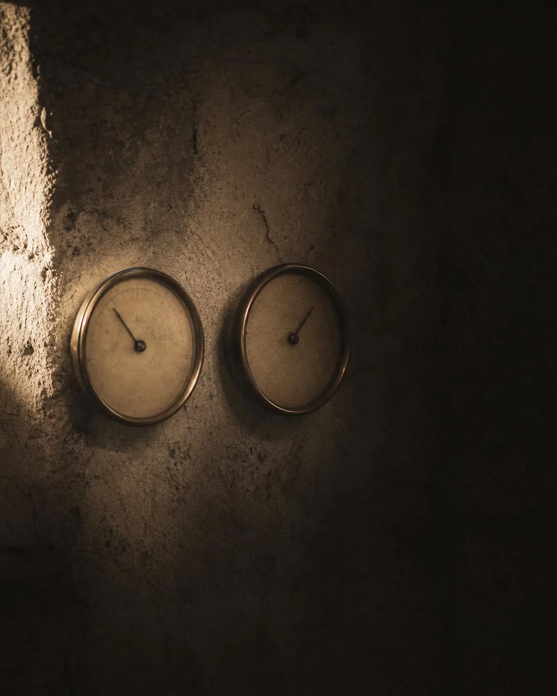 Two aged analogue dials on a stone cellar wall in low light.