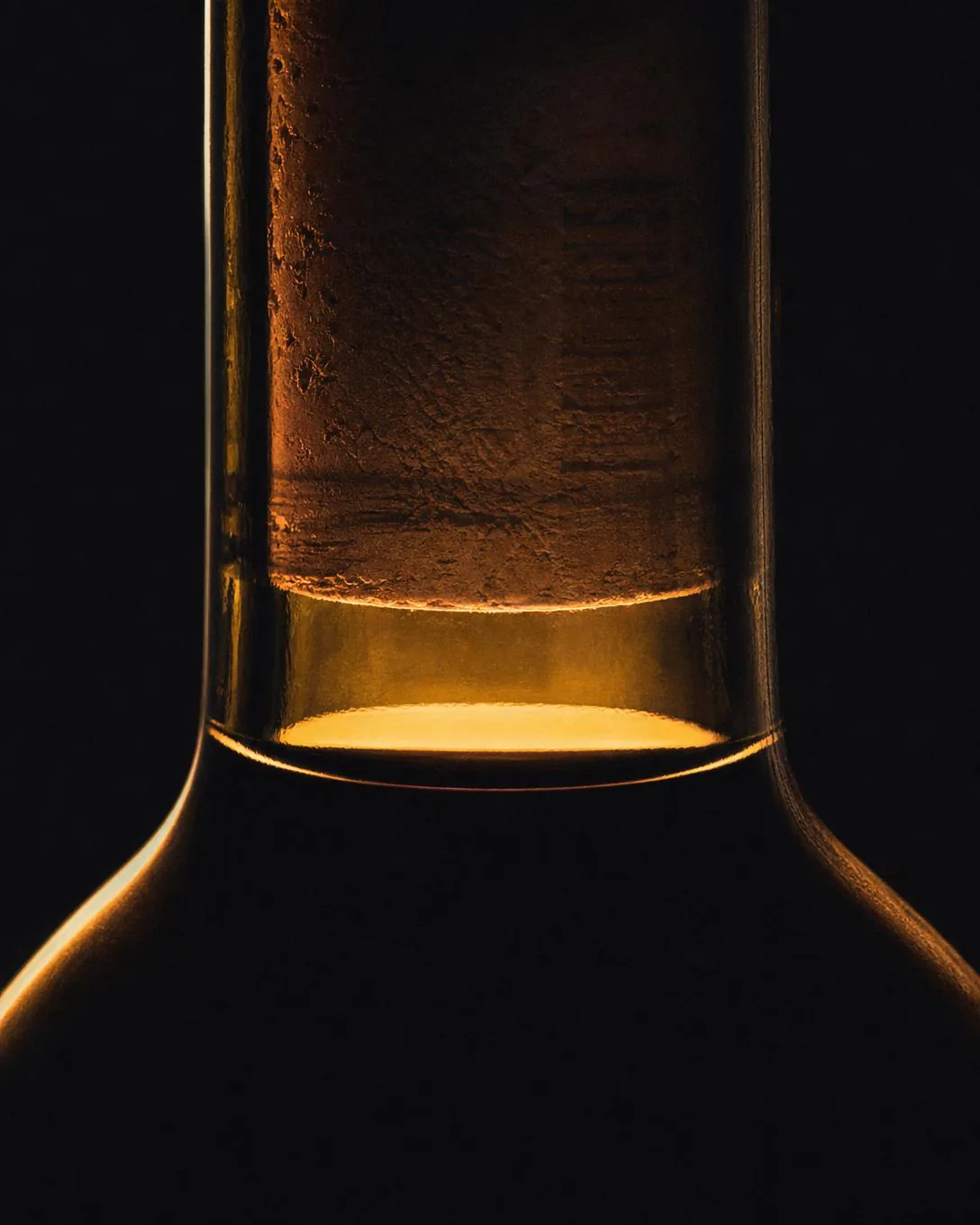 Backlit bottle neck showing the air gap between cork and wine — the ullage.