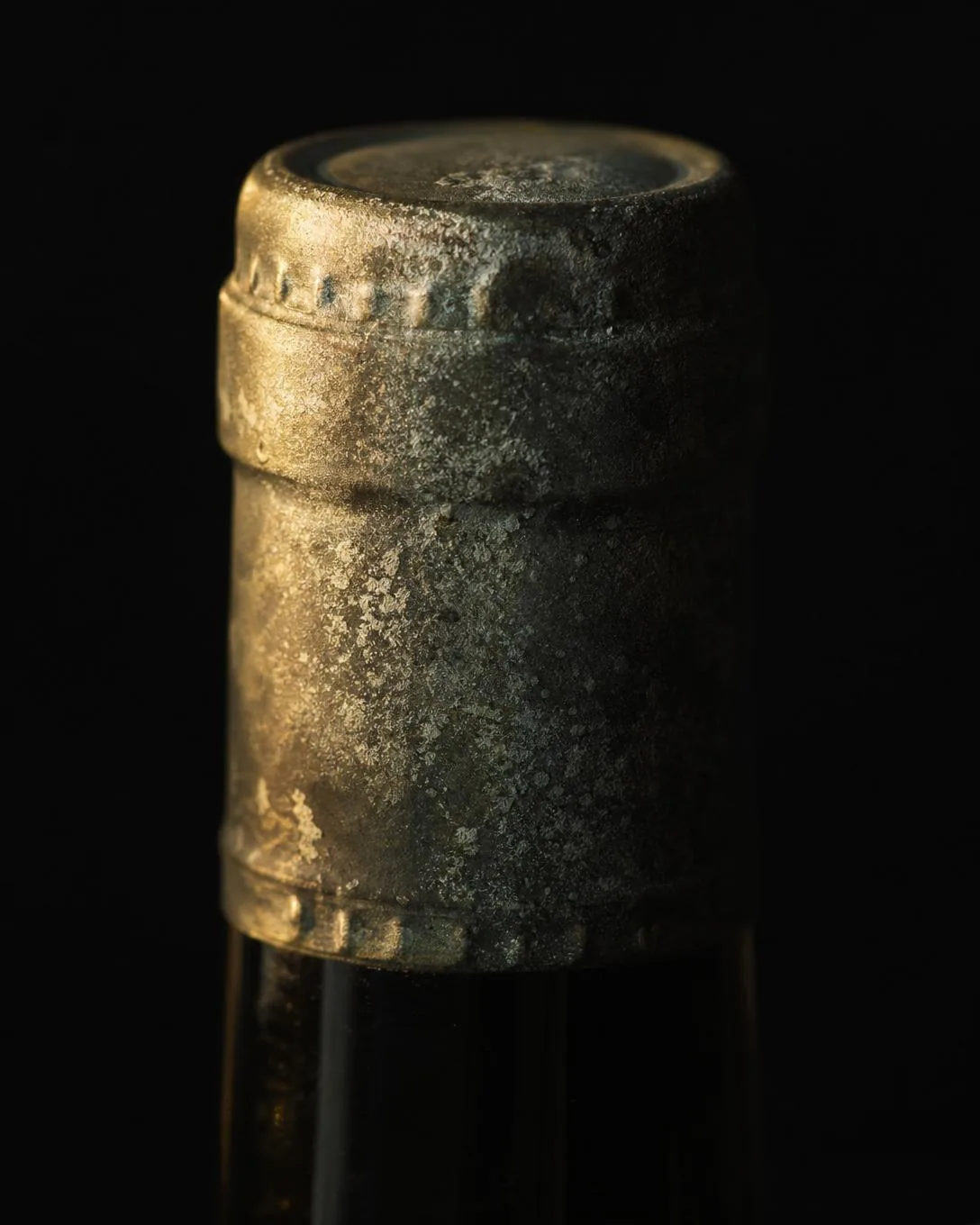 An aged tin capsule with a fine pale bloom of oxidation and dulled patina across the metal.