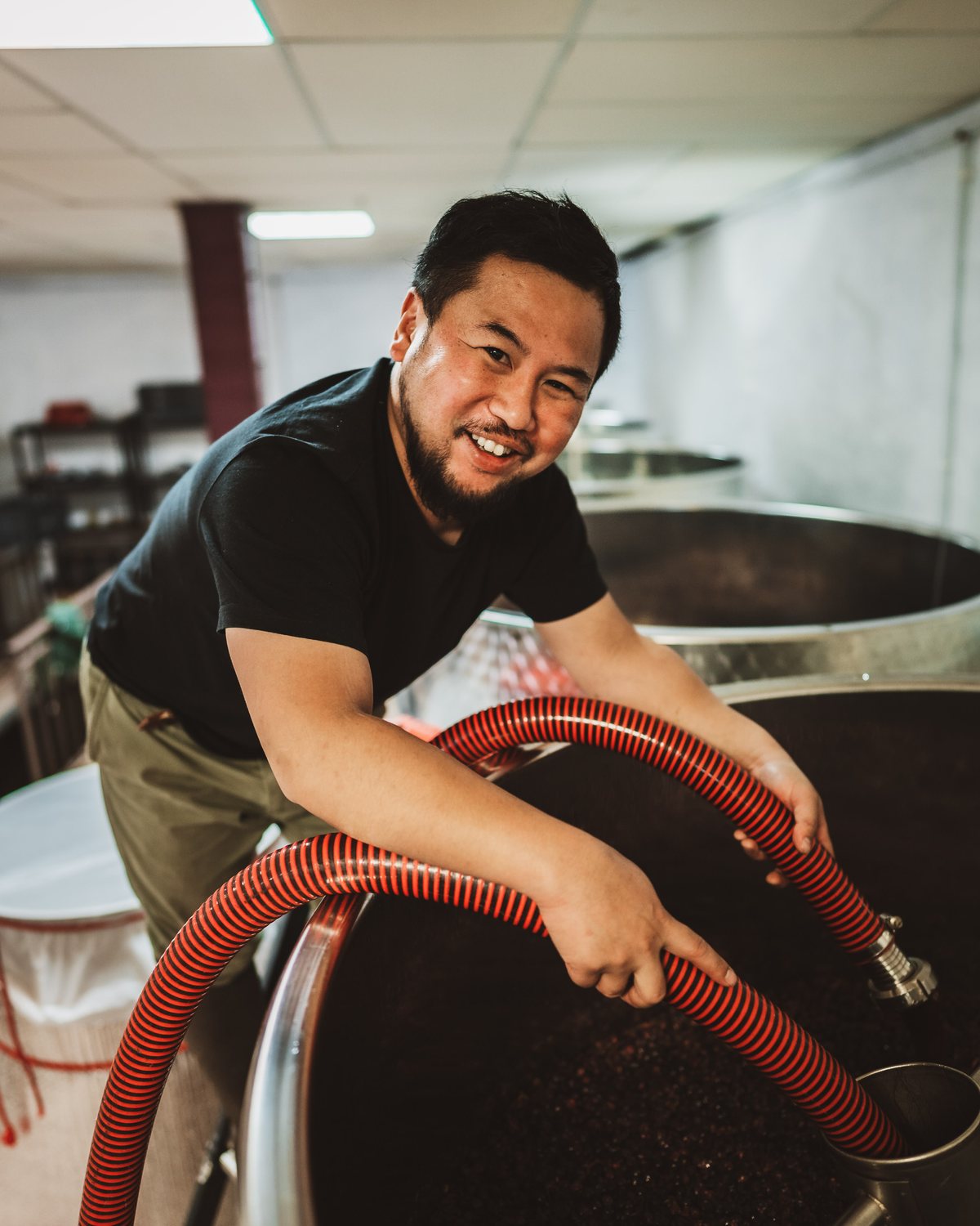 Hirotaka Ito, winemaker of Domaine Kuheiji, smiling over an open tank while guiding the pumping-over hose in the cuverie.